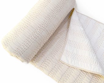 May include: A white cotton quilt with a subtle pink stitching pattern. The quilt is rolled up and partially unfurled, showcasing the intricate stitching detail.