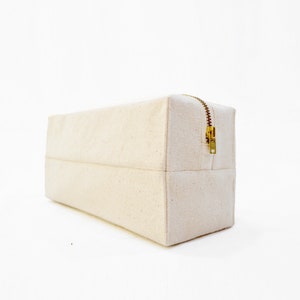 May include: A rectangular, off-white canvas zippered pouch with a gold zipper.