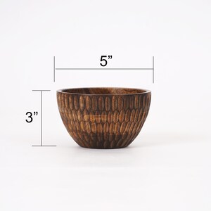 May include: A small, dark brown wooden bowl with a textured, patterned surface. The bowl is 5 inches wide and 3 inches tall.