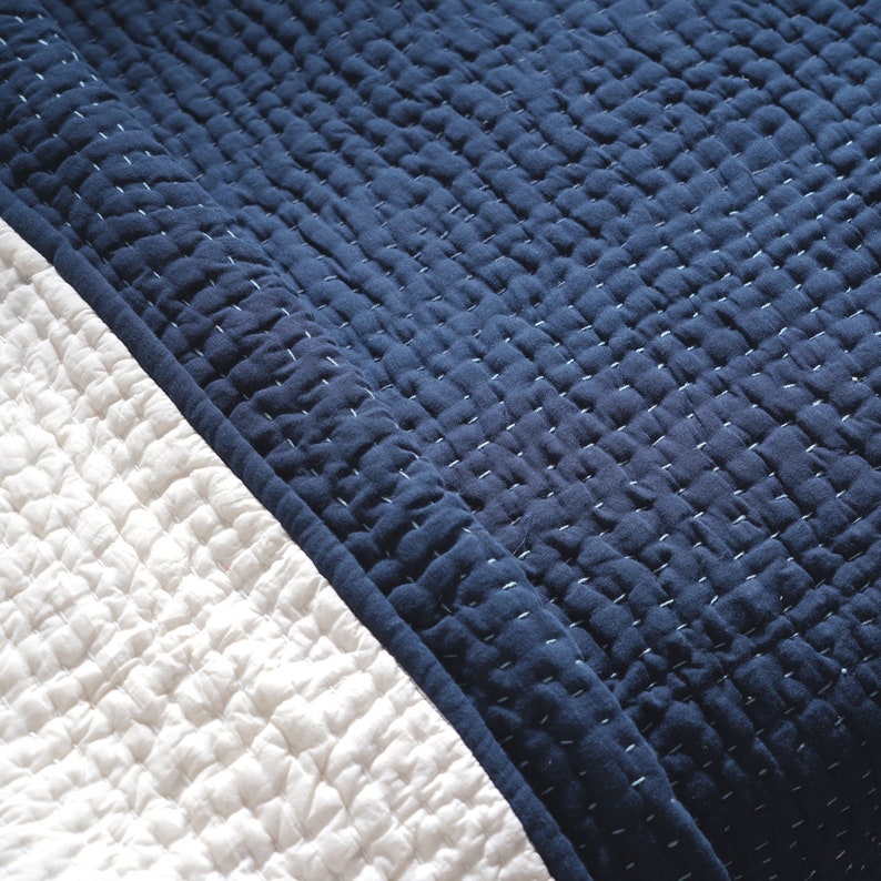 May include: Close-up of a navy blue and white quilted blanket. The navy blue section is on the top right, with a white section on the bottom left. The blanket has a textured, stitched pattern.
