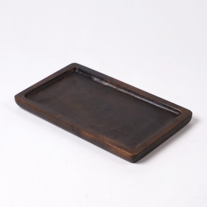May include: A rectangular wooden tray with a dark brown finish. The tray has a raised edge and a smooth surface.