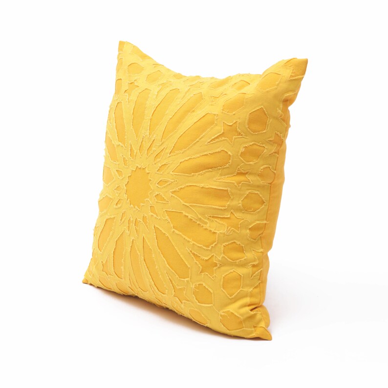 Pu&ograve; includere: Un cuscino quadrato giallo caratterizzato da un motivo geometrico complesso e prominente con forme a stella e poligoni. Il design &egrave; realizzato con ritagli di tessuto sovrapposti dai bordi sfilacciati, che conferiscono un aspetto strutturato.
