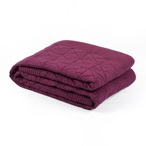 May include: A folded purple quilted throw blanket with a diamond pattern.