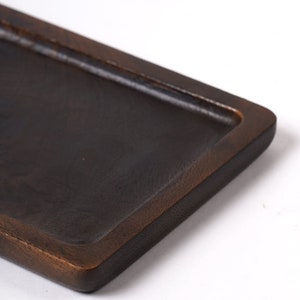 May include: A dark brown wooden tray with a slightly raised edge. The tray is rectangular and has a smooth, polished surface.