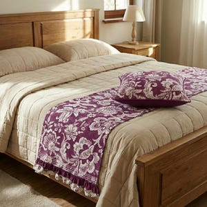 Può includere: Un letto con struttura in legno e una trapunta beige trapuntata. Un runner decorativo viola con un motivo floreale e un cuscino abbinato sono posizionati sul letto. Il runner ha un bordo a balze.