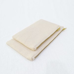 May include: Two beige canvas zipper pouches stacked on top of each other. The pouches have gold zippers.