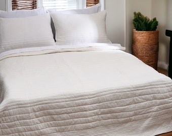 May include: A white, quilted bedspread with a subtle, horizontal pattern. The bedspread is on a bed with two white pillows.