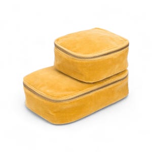 May include: Two mustard yellow velvet zippered pouches, one stacked on top of the other.