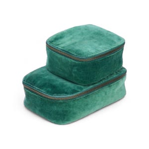 May include: Two green velvet zippered pouches stacked on top of each other. The pouches are made of a soft, plush fabric and have a subtle sheen.