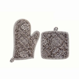 May include: A brown oven mitt and pot holder set. Both items feature a white floral pattern on a quilted background. The edges are trimmed with a white and brown striped border. The pot holder has a loop for hanging.