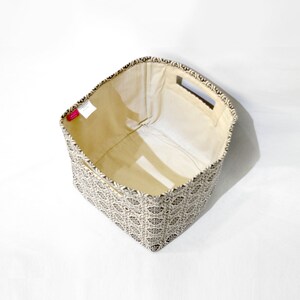 May include: An empty fabric storage bin with a black and white geometric pattern. The bin has a beige lining and two cut-out handles on the top.