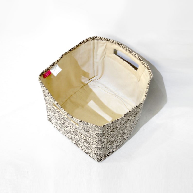 May include: An empty fabric storage bin with a black and white geometric pattern. The bin has a beige lining and two cut-out handles on the top.