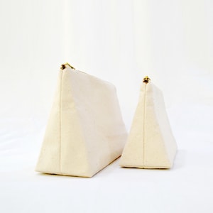 May include: Two off-white canvas zippered pouches in a triangular shape. The larger pouch is behind the smaller pouch.