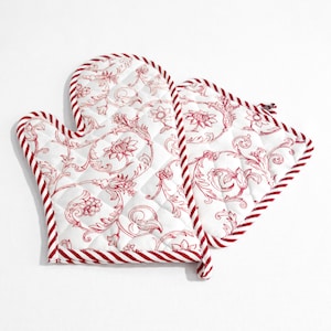 Peut inclure: Une paire de maniques de cuisine matelassées rouge et blanc avec un motif floral. Les maniques ont une bordure rayée.
