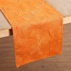 Op de afbeelding: Oranje tafelkleed met een geometrisch patroon van gouden gebogen lijnen.