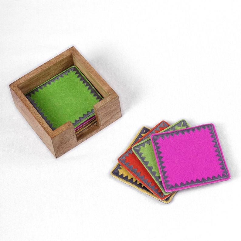 Peut inclure: Un ensemble de six sous-verres color&eacute;s avec un bord festonn&eacute; gris. Les sous-verres sont empil&eacute;s et dispos&eacute;s dans un porte-sous-verres en bois.