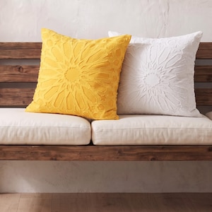 Pu&ograve; includere: Due cuscini quadrati, uno giallo brillante e uno bianco, ciascuno caratterizzato da un intricato motivo geometrico a stella in rilievo sulla superficie anteriore. I cuscini sono posizionati fianco a fianco e mostrano un design testurizzato.