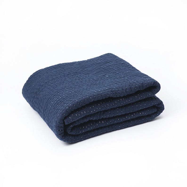 May include: Folded navy blue quilt with white stitching. The quilt is made of a textured fabric and is folded neatly, showcasing its layered construction. The stitching creates a subtle pattern across the surface.