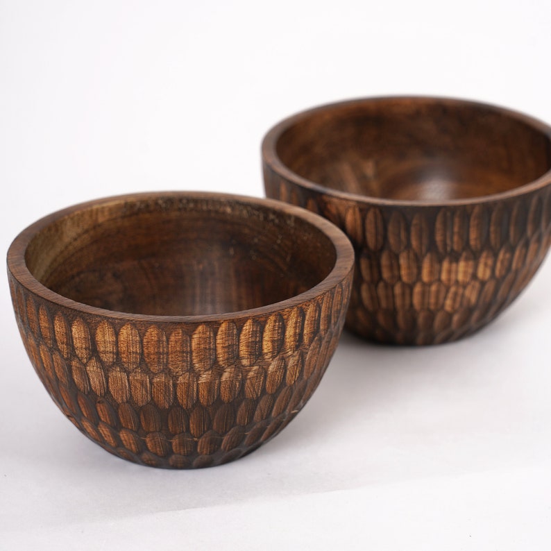 May include: Two wooden bowls with a dark brown finish. The bowls have a unique design with a pattern of small, oval-shaped indentations.