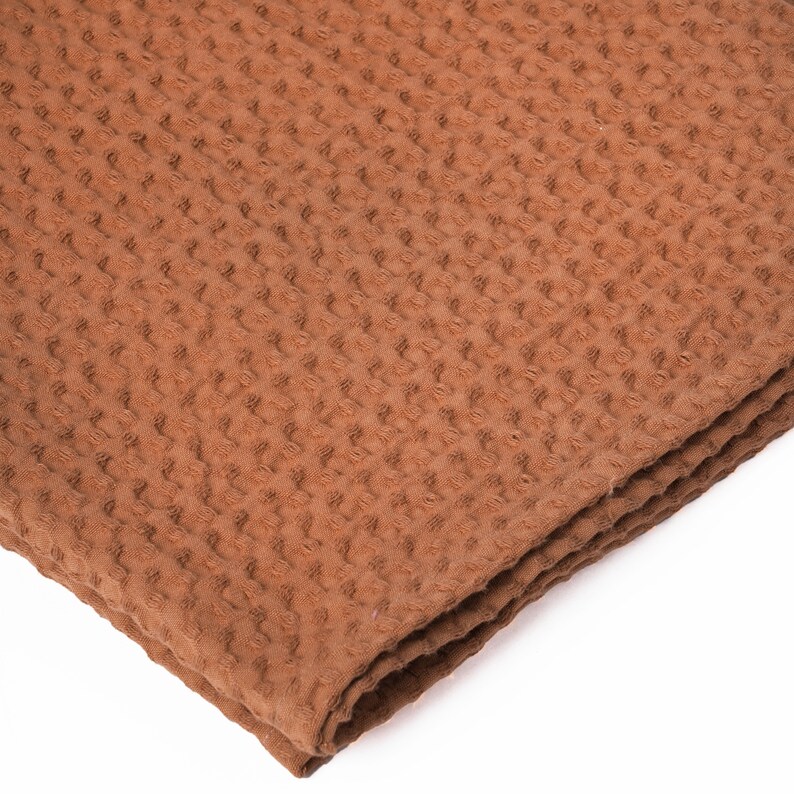 Puede incluir: Una toalla de tejido de waffle marr&oacute;n doblada en tres. La toalla est&aacute; hecha de un material suave y absorbente.