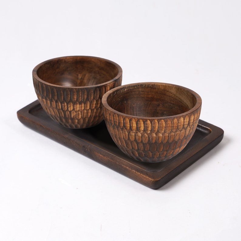 May include: Two dark brown wooden bowls with a textured pattern sit on a dark brown wooden tray. The bowls are empty.