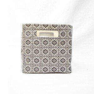 May include: A black and white patterned fabric storage bin with a cut-out handle. The bin is made of a sturdy fabric and has a rectangular shape.