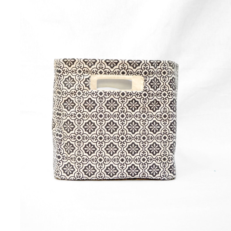 May include: A black and white patterned fabric storage bin with a cut-out handle. The bin is made of a sturdy fabric and has a rectangular shape.
