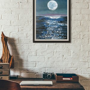 May include: Framed painting of a moonlit ocean scene. The artwork features a large, bright white moon in a dark blue sky, reflecting on the water. The water is a mix of dark and light blues with white highlights, creating a shimmering effect.