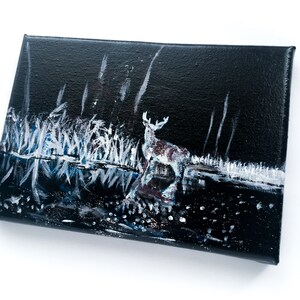 May include: An original painting on canvas depicts a deer standing near water at night. The artwork features a dark background with white and blue accents representing the water and foliage. The deer is painted with shades of brown and white.