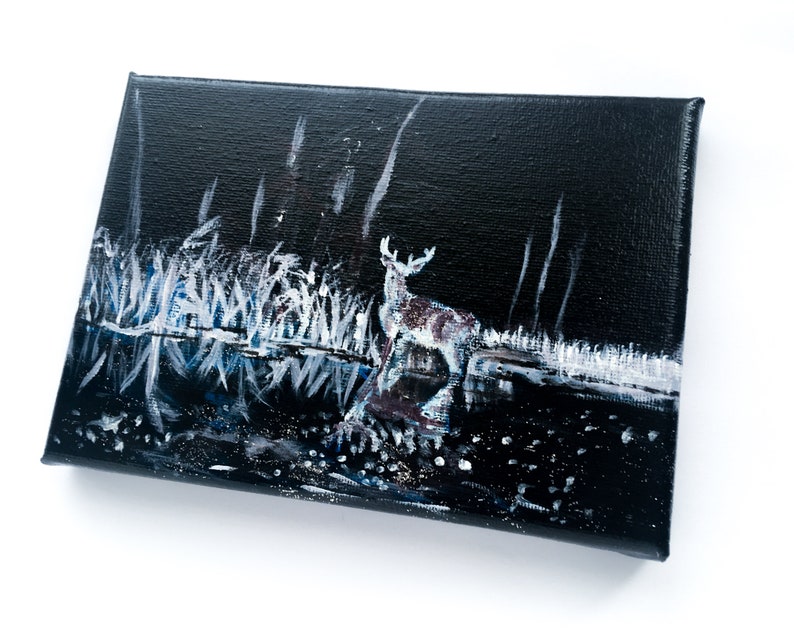 May include: An original painting on canvas depicts a deer standing near water at night. The artwork features a dark background with white and blue accents representing the water and foliage. The deer is painted with shades of brown and white.