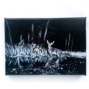 May include: An acrylic painting on canvas depicts a deer standing in a dark, moonlit forest. The artwork features a black background with white and blue highlights, creating a reflective water effect. The deer is brown and white.