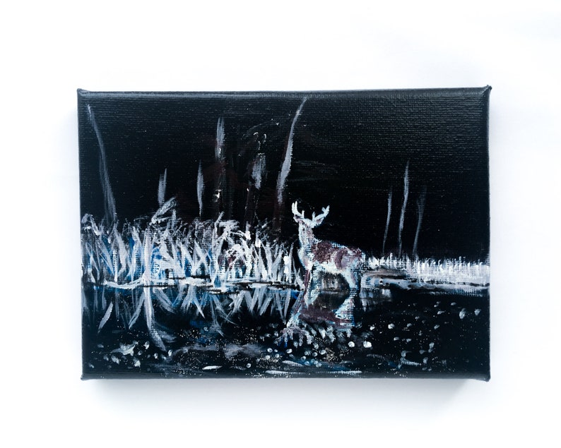 May include: An acrylic painting on canvas depicts a deer standing in a dark, moonlit forest. The artwork features a black background with white and blue highlights, creating a reflective water effect. The deer is brown and white.