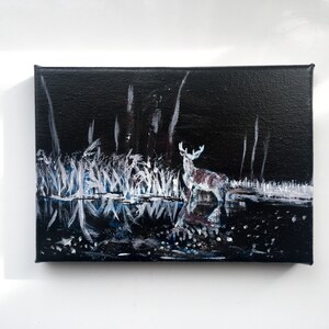 May include: An acrylic painting on canvas depicts a deer standing in a dark, reflective body of water. The artwork features white and blue brushstrokes representing tall grass and trees against a black background. The deer has white antlers and brown spots.