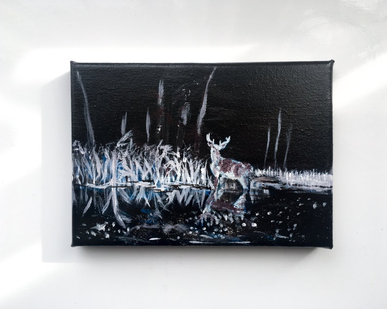 May include: An acrylic painting on canvas depicts a deer standing in a dark, reflective body of water. The artwork features white and blue brushstrokes representing tall grass and trees against a black background. The deer has white antlers and brown spots.