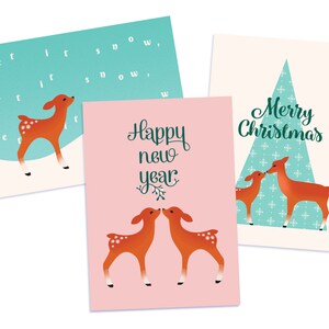 May include: Three Christmas cards featuring a deer design. The first card is blue with the text "Let it snow, let it snow, let it snow". The second card is pink with the text "Happy New Year". The third card is cream with a blue and white patterned Christmas tree and the text "Merry Christmas".