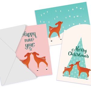 May include: Set of three Christmas cards featuring a deer design. The first card is pink with two deer kissing. The second card is green with a single deer and the text "let it snow". The third card is cream with a Christmas tree and two deer kissing. The text "Merry Christmas" is on the card.