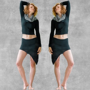 May include: A black long-sleeve crop top and matching asymmetrical mini skirt. The outfit includes a gray cowl neck scarf. The model is standing in front of a gray background.