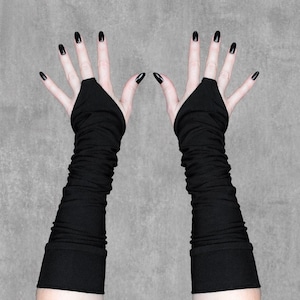 May include: A pair of black fingerless gloves with long sleeves. The gloves are made of a soft, stretchy material and have a ruched design. The nails are painted black.