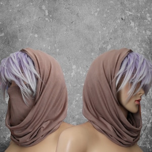 Peut inclure: Deux mannequins portent des voiles de t&ecirc;te de couleur taupe. Le tissu enveloppe la t&ecirc;te et le cou, couvrant partiellement le visage. Les mannequins ont la peau p&acirc;le, les l&egrave;vres rouges et des cheveux violets clair et blancs. Le fond est un mur gris textur&eacute;.