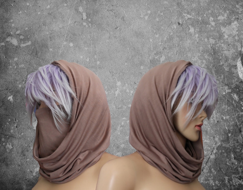 Peut inclure: Deux mannequins portent des voiles de t&ecirc;te de couleur taupe. Le tissu enveloppe la t&ecirc;te et le cou, couvrant partiellement le visage. Les mannequins ont la peau p&acirc;le, les l&egrave;vres rouges et des cheveux violets clair et blancs. Le fond est un mur gris textur&eacute;.
