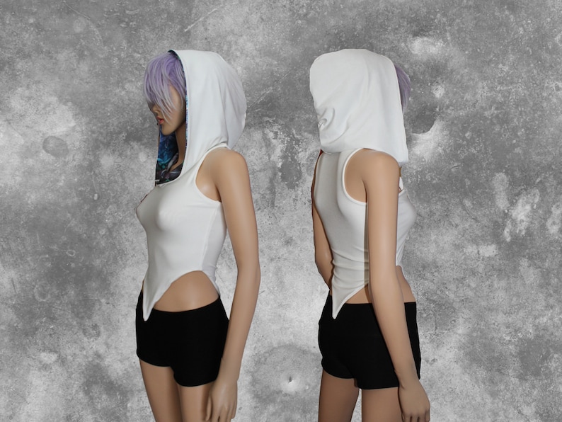 Puede incluir: Top blanco sin mangas con cuello de capucha blanco. La parte superior tiene un dobladillo largo y puntiagudo a cada lado. La modelo lleva pantalones cortos negros.