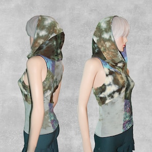 May include: A sleeveless top with a large, attached hood. The top is made of a patchwork of different fabrics in shades of green, brown, and white. The hood is a cowl style and is gathered at the neck.