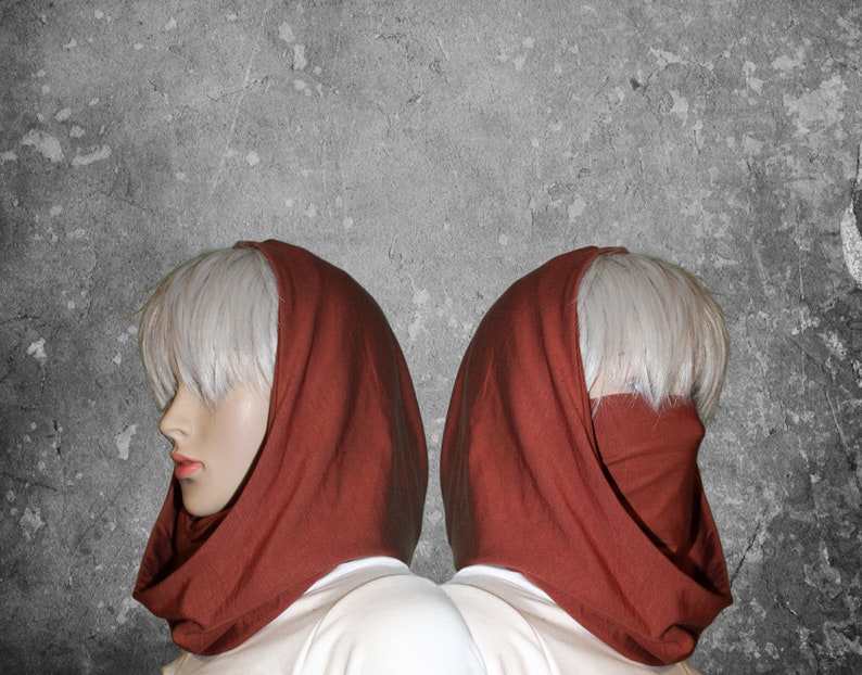 Peut inclure: Deux mannequins portent des capuches de couleur rouille. Les capuches sont faites d'un tissu doux et couvrent la t&ecirc;te et le cou, avec la possibilit&eacute; de couvrir le bas du visage. Les mannequins ont la peau p&acirc;le et les cheveux courts et clairs. Le fond est un mur gris textur&eacute;.