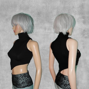 May include: A black sleeveless turtleneck top with a high neckline and a cropped hem. The top is asymmetrical, with one side longer than the other. The top is shown on a mannequin with silver hair.