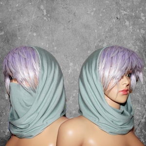 Peut inclure: Deux mannequins avec des perruques violet clair et des foulards verts clairs. Les foulards sont drap&eacute;s autour du cou et couvrent le bas du visage d'un mannequin. Le fond est un mur gris textur&eacute;.