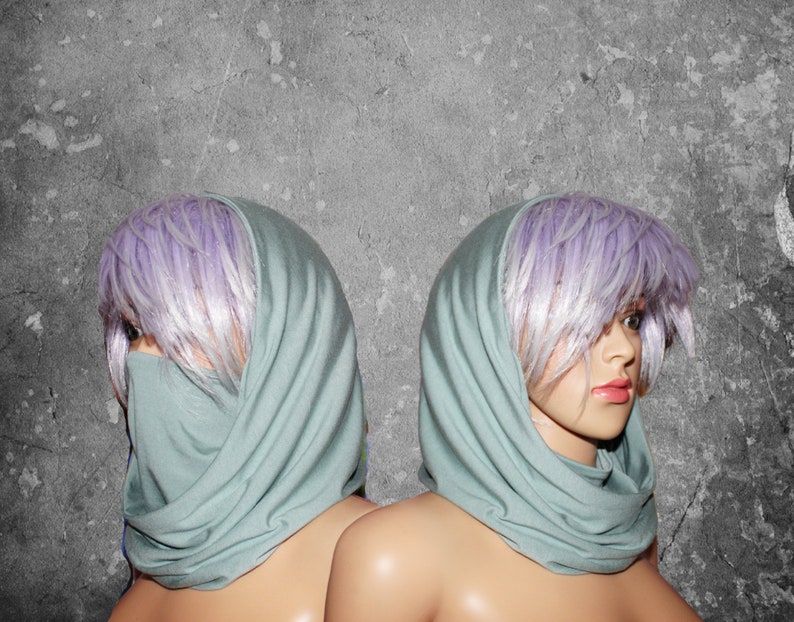 Peut inclure: Deux mannequins avec des perruques violet clair et des foulards verts clairs. Les foulards sont drap&eacute;s autour du cou et couvrent le bas du visage d'un mannequin. Le fond est un mur gris textur&eacute;.