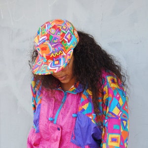Female model wearing pink Fresh prince hat with thrifted 90s windbreaker in pink with ripped blue shorts.