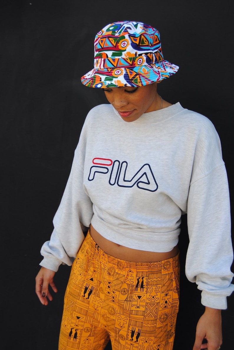 Model wearing vintage FILA sweatshirt and white bucket hat with colorful 90s abstract design.