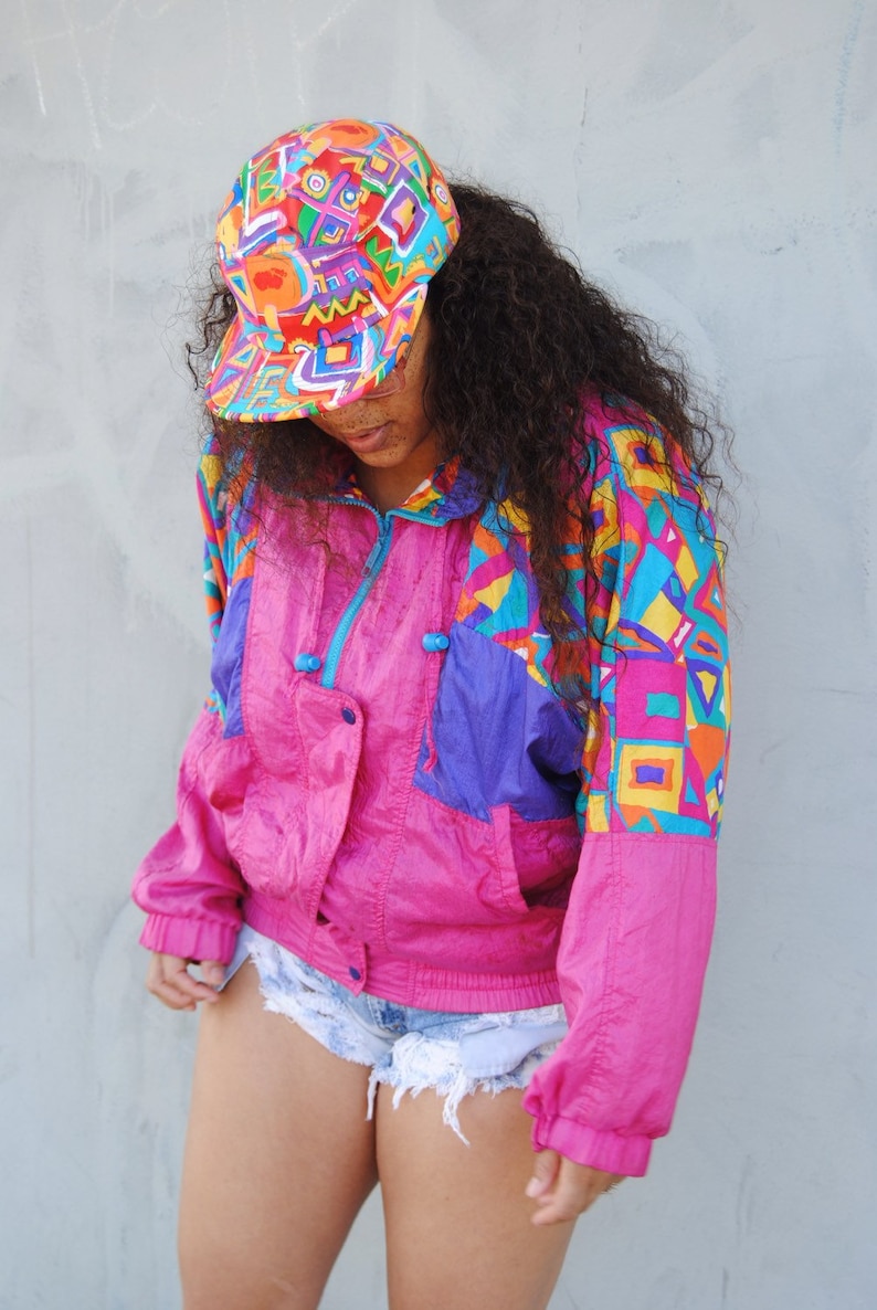 Female model wearing pink Fresh prince hat with thrifted 90s windbreaker in pink with ripped blue shorts.