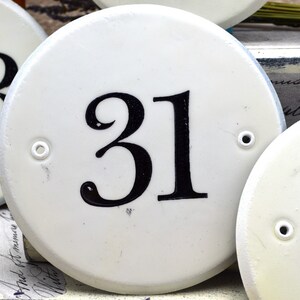 May include: Three white ceramic house number plaques with black numbers. The numbers are 53, 31, and 2. The plaques have a small hole on each side.